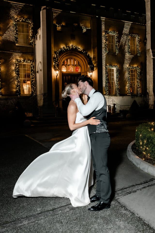Bride and groom share a kiss outside illuminated Bellingham Castle at night.
