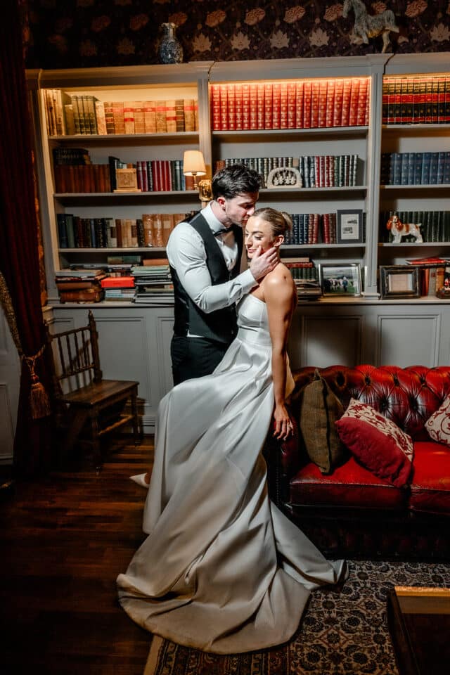 Bride and groom embrace tenderly in a cozy library setting at Bellingham Castle.