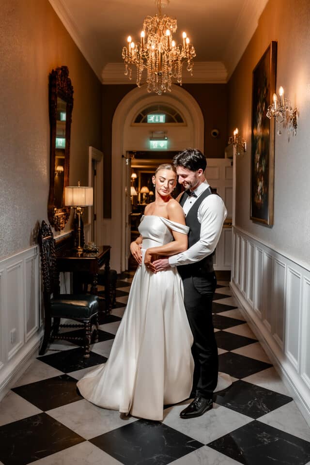Bride and groom embracing in an elegant hallway at Bellingham Castle.