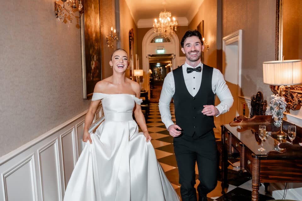 Bride and groom joyfully walking through an elegant hallway at Bellingham Castle.