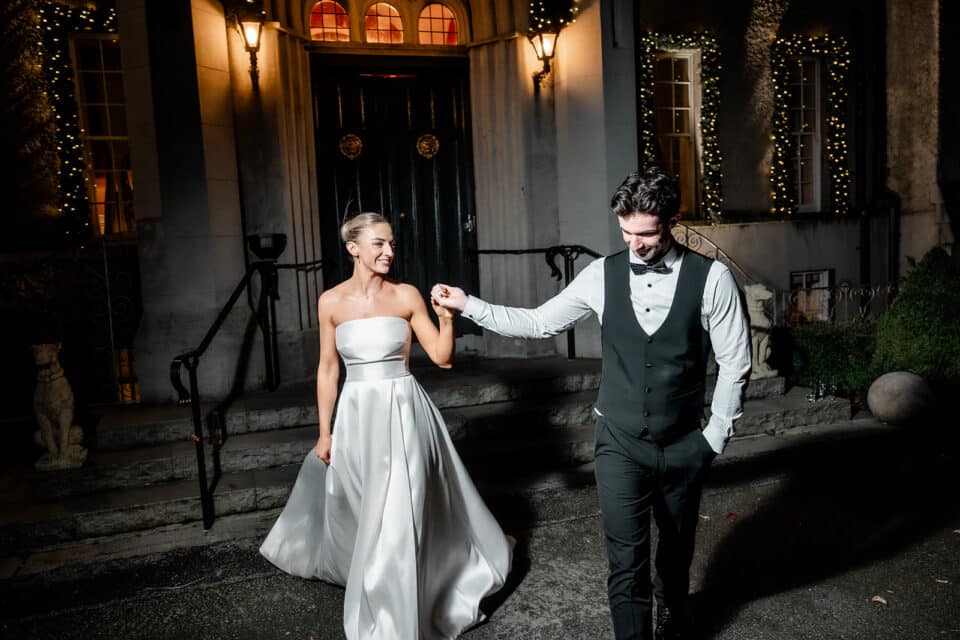 Couple smiling and holding hands outside a lit castle entrance at night.