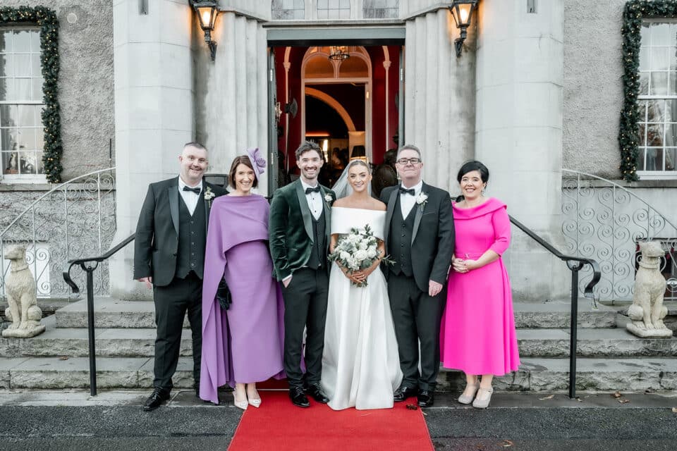 Bride and groom with family and friends outside Bellingham Castle on a red carpet.