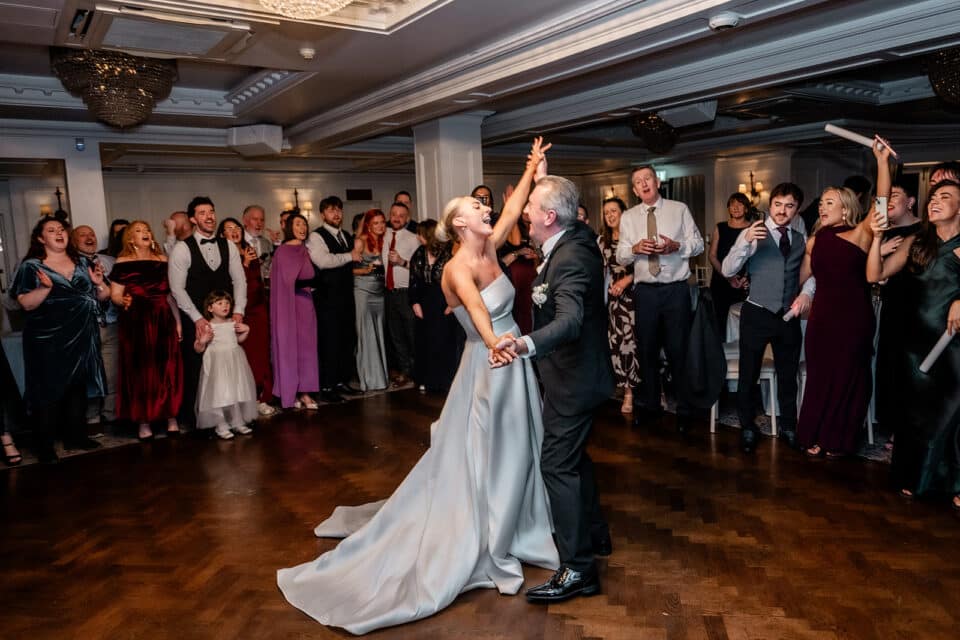 Bride and groom dancing joyfully amidst cheering guests at Bellingham Castle.