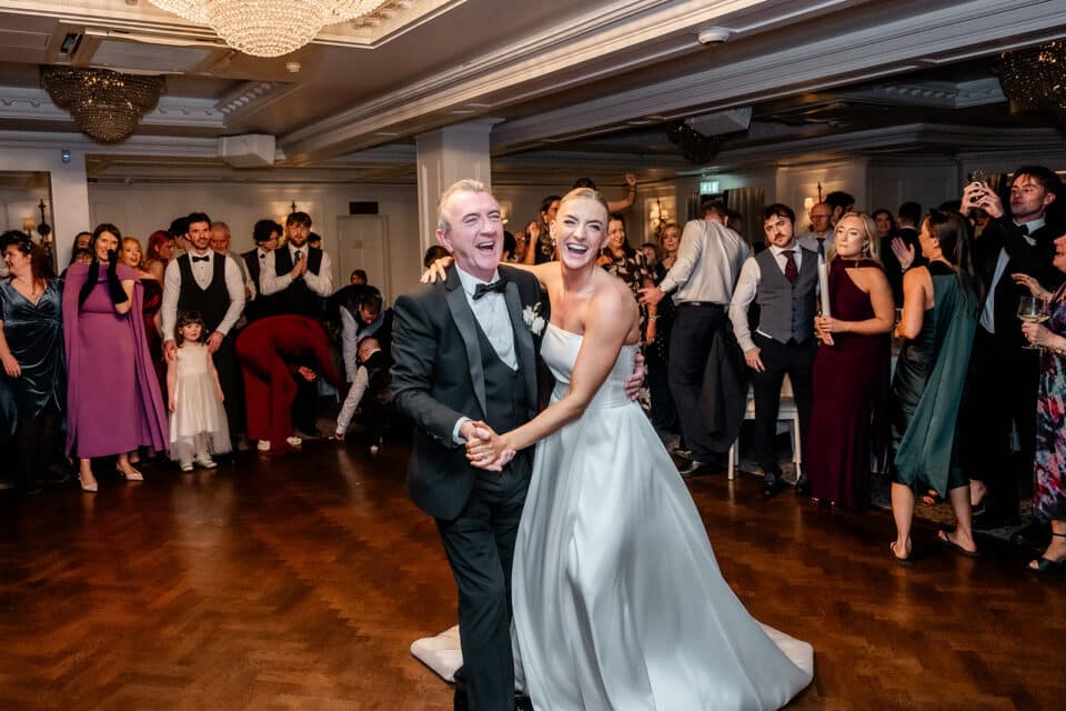 Bride and groom dancing joyfully at a wedding reception with guests watching.
