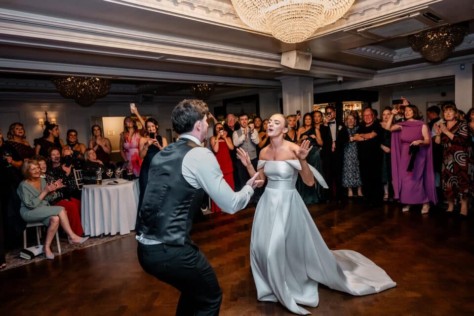 Bride and groom dancing joyfully at their wedding reception in Bellingham Castle, surrounded by cheering guests.