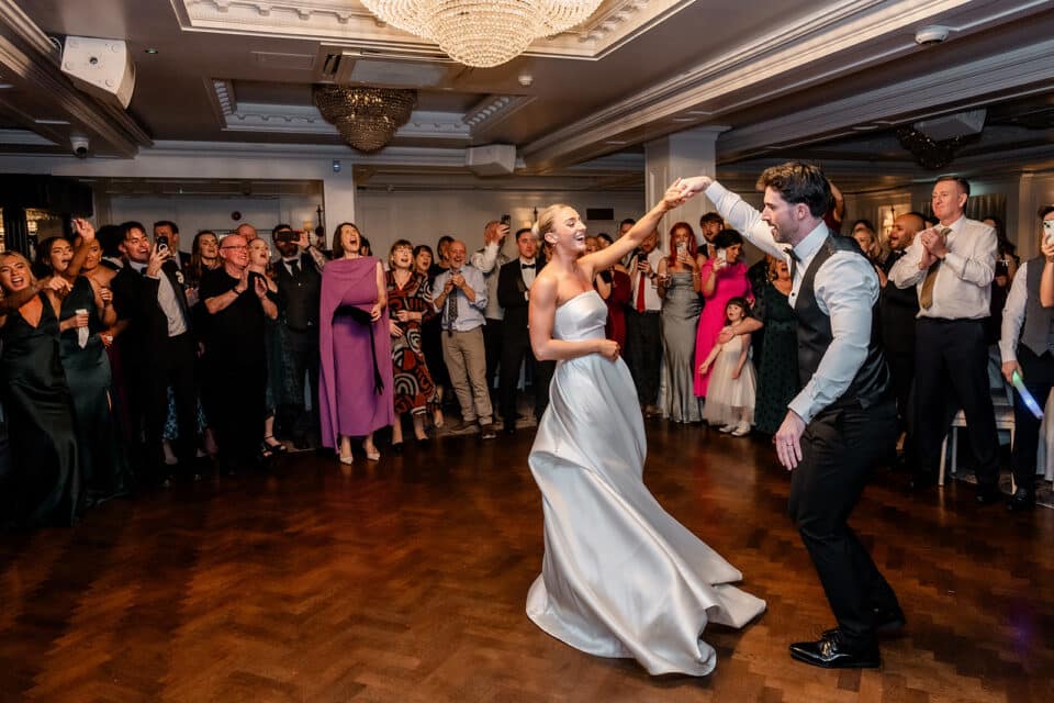 Bride and groom dancing at wedding reception with cheering guests at Bellingham Castle.