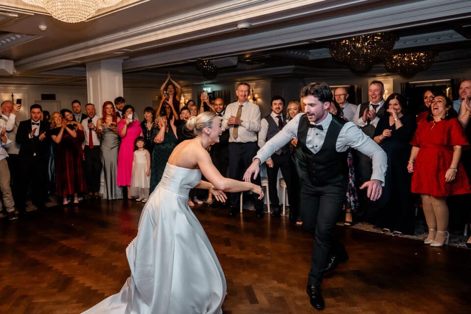 Bride and groom dancing energetically at wedding reception with an enthusiastic crowd cheering at Bellingham Castle.