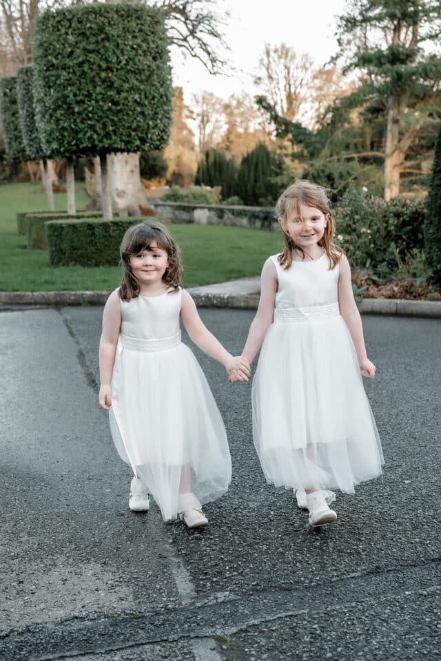 Two young girls in white dresses holding hands at Bellingham Castle garden.