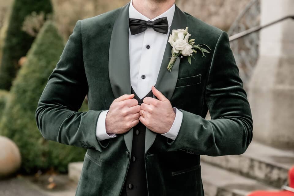 Man in green velvet tuxedo with white rose boutonniere adjusting suit.