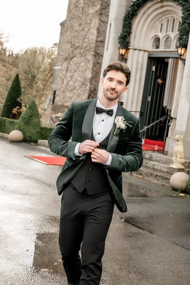Man in a green velvet tuxedo walking outside Bellingham Castle.