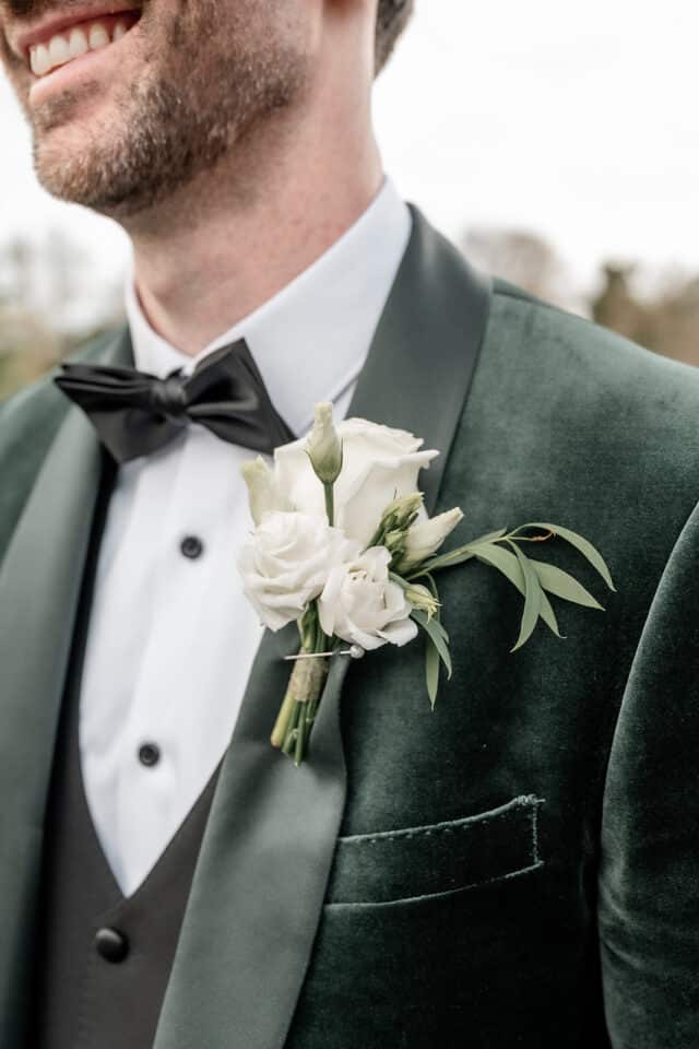 Groom in a green velvet tuxedo with white floral boutonniere and black bow tie.