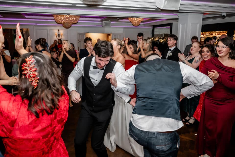 Guests dancing and celebrating at a lively wedding reception in a decorated ballroom.