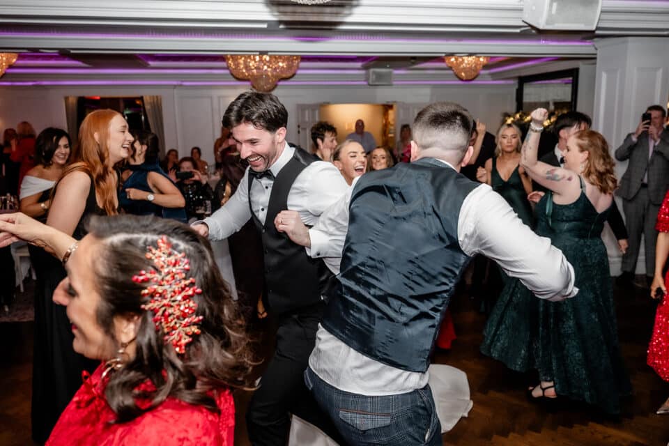 Guests dancing joyfully at a wedding reception in an elegant venue with chandeliers.