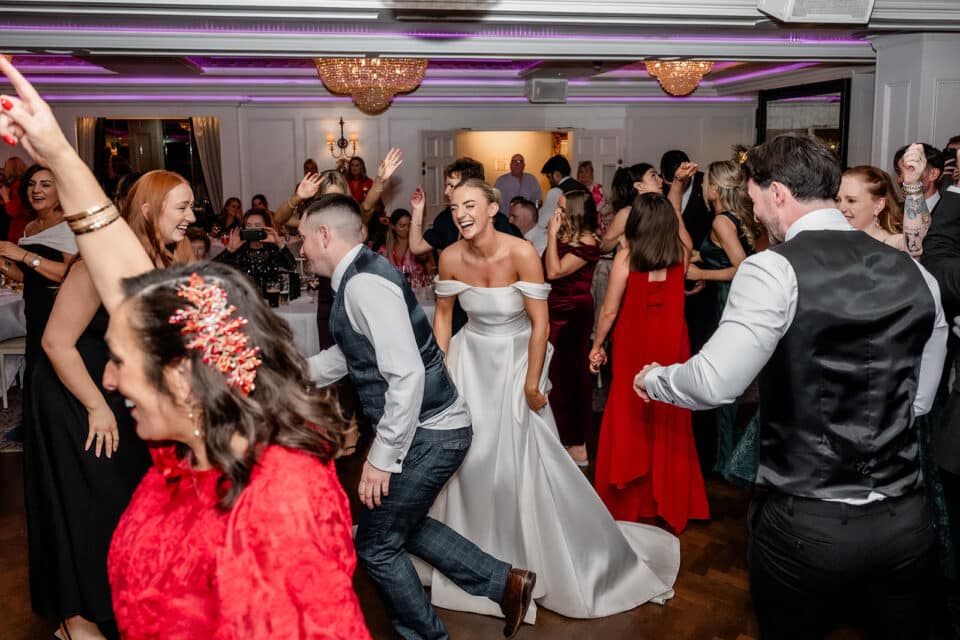 Wedding celebration with guests dancing at Bellingham Castle, featuring a bride in a white gown joyfully interacting with attendees.