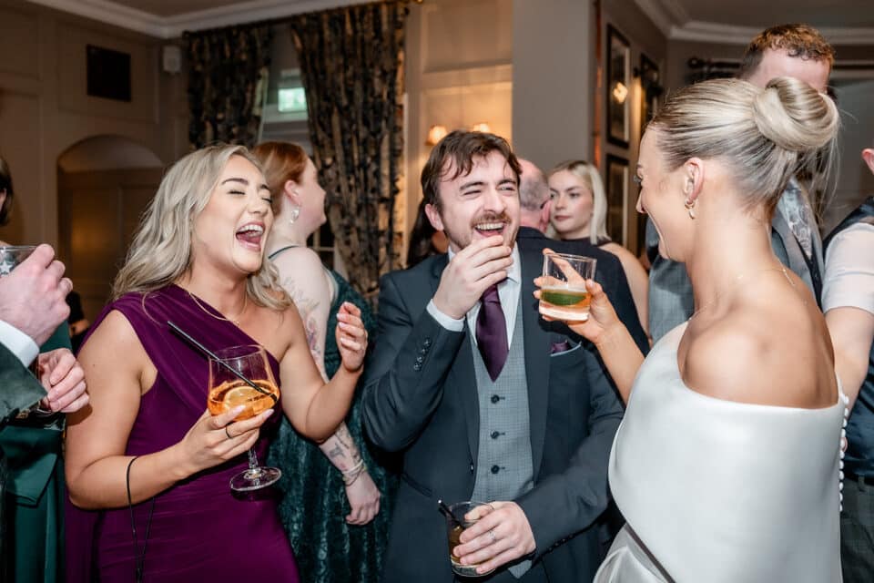 Wedding guests laughing and enjoying drinks indoors, Bellingham Castle.
