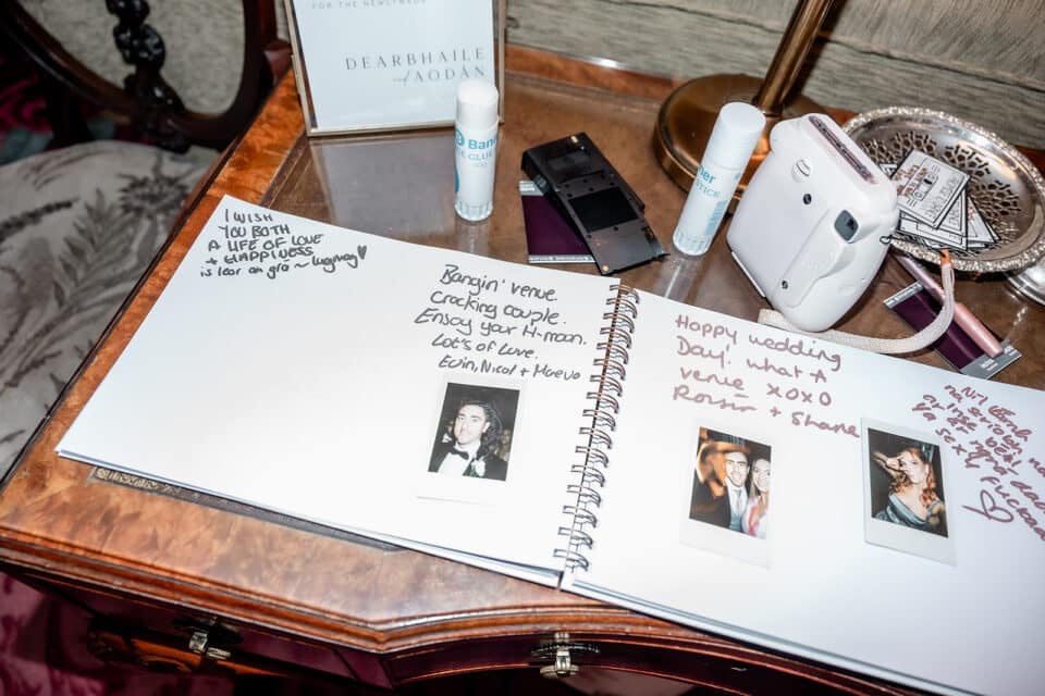 Wedding guest book with messages, instant photos, and a camera on a wooden table.