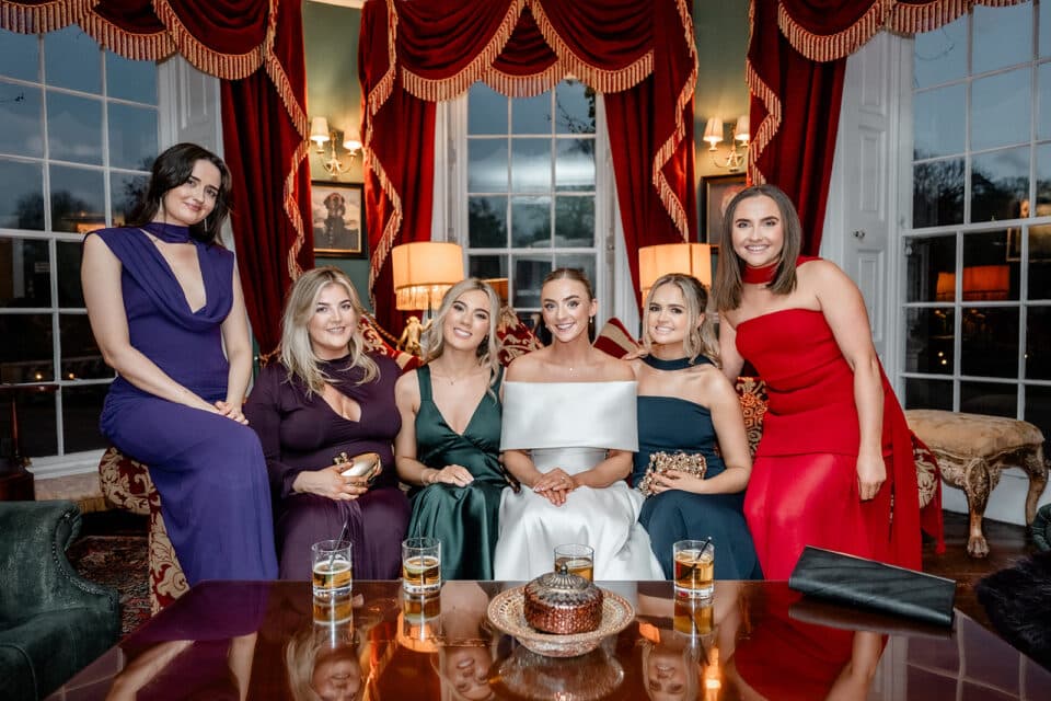 Group of women in elegant evening dresses sitting in a lavishly decorated room at Bellingham Castle.
