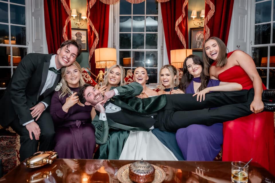Group of friends celebrating at Bellingham Castle, with one person being playfully held horizontally.