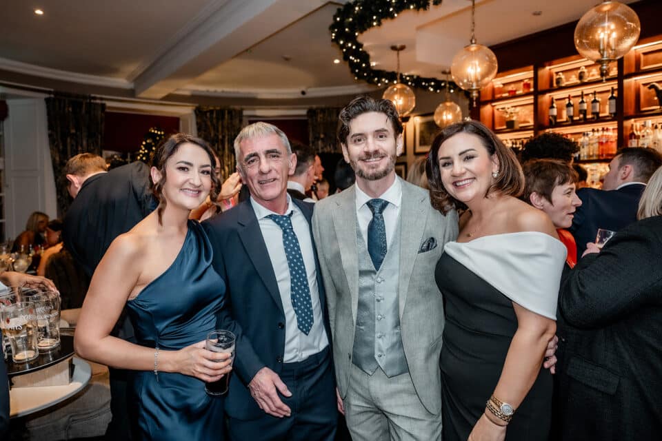 Group of four people posing at a festive indoor event, elegantly dressed.
