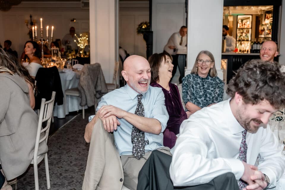 Guests laughing at a wedding reception in Bellingham Castle, with a warmly lit and elegant setting in the background.
