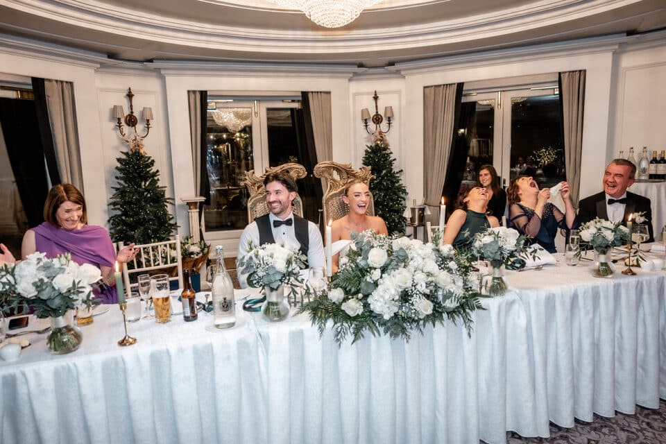 Wedding party laughing at the head table with floral decorations at Bellingham Castle.