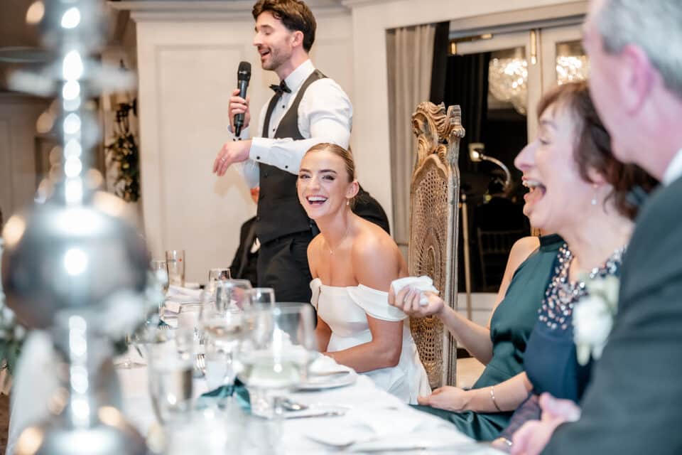 A wedding reception speech with the bride smiling and guests laughing at Bellingham Castle.
