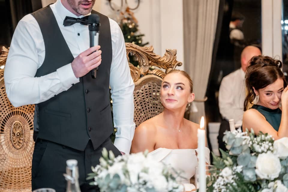 Wedding speech at Bellingham Castle with bride and groom seated, surrounded by elegant decor and floral arrangements.