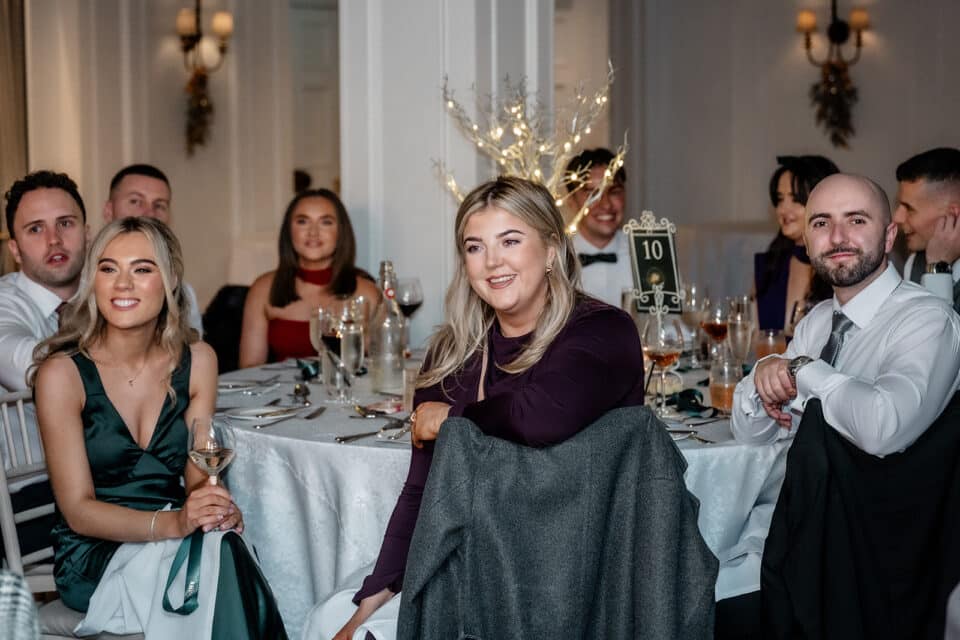 Guests seated at a wedding reception, smiling and engaged around a decorated table setting.