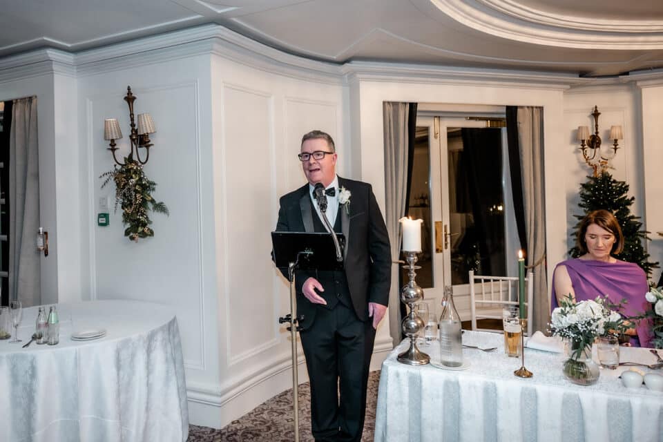 Man giving speech at wedding reception in elegantly decorated venue.