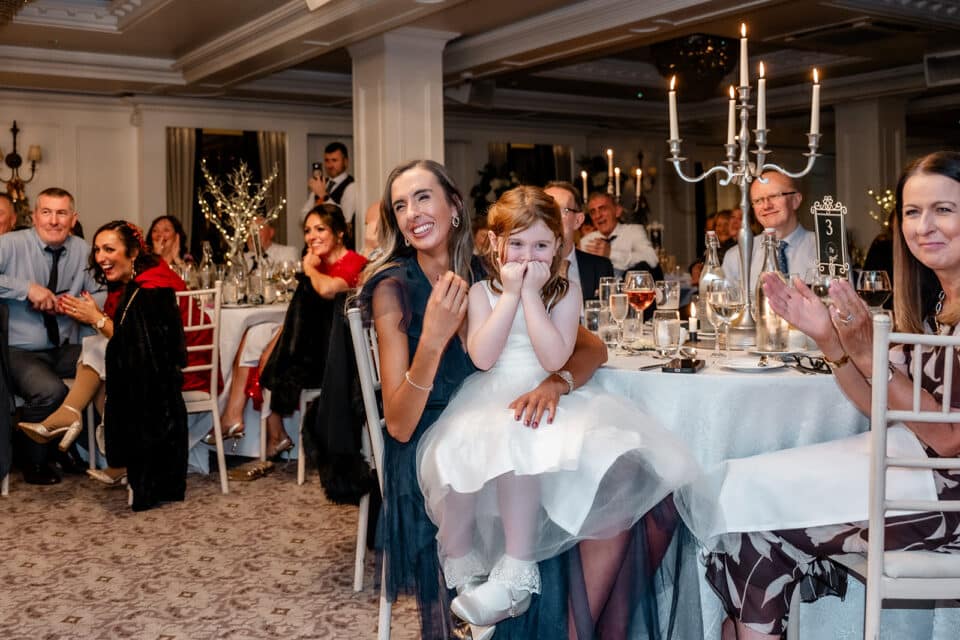 Guests smiling and applauding at a wedding reception at Bellingham Castle, with elegant decor and candlelit centerpieces.