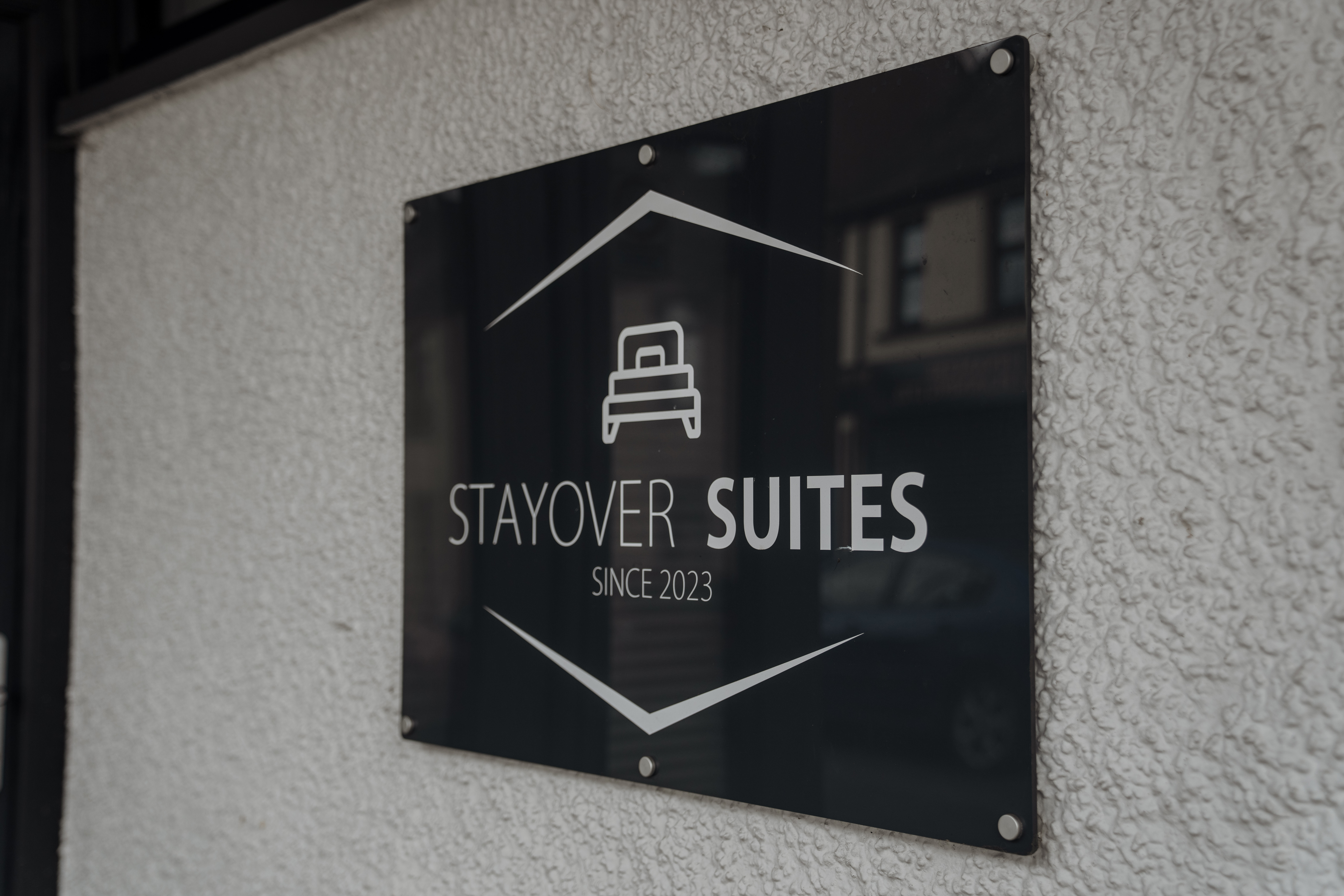 Sign reading "Stayover Suites Since 2023" with a bed icon on a textured wall.