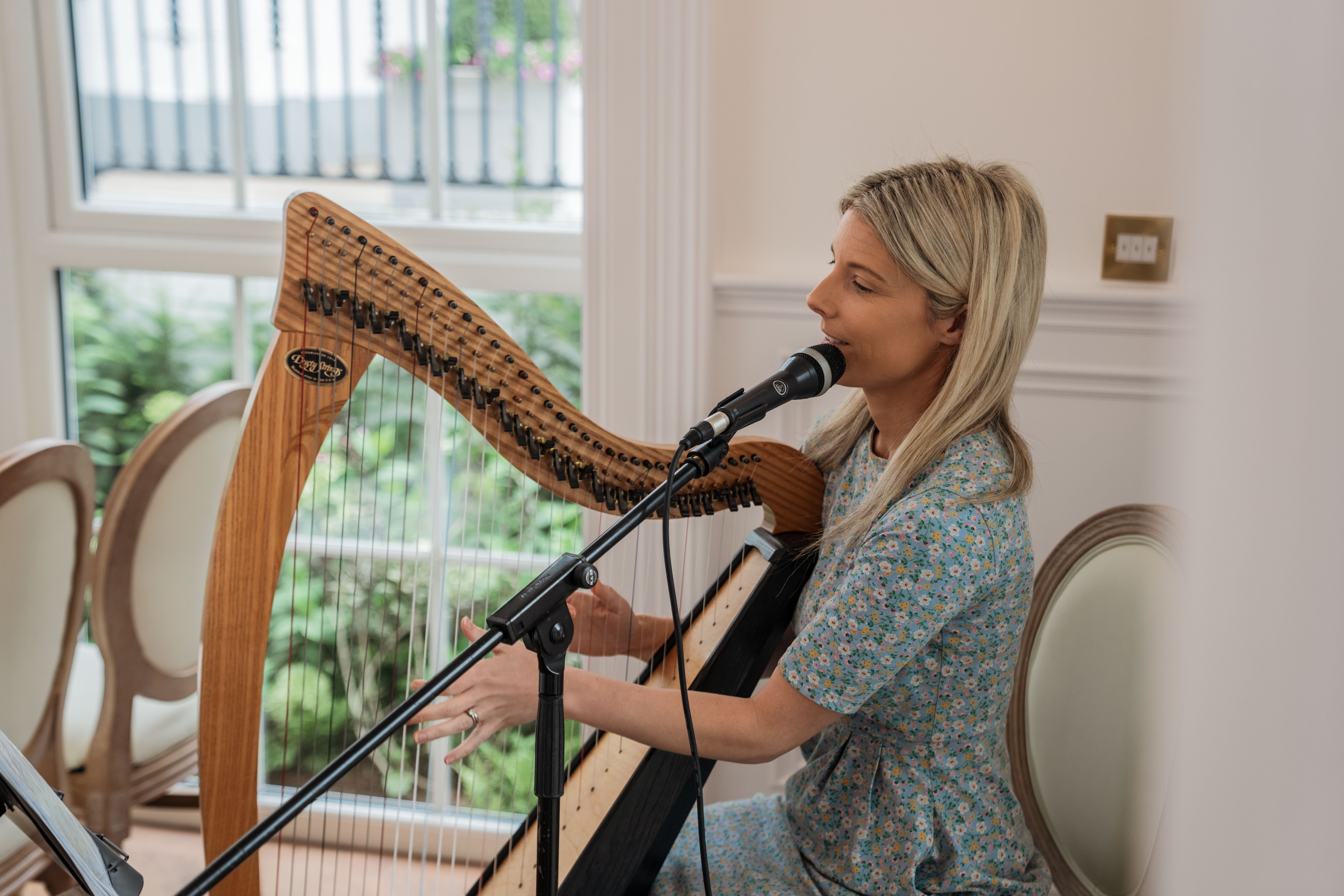 Woman playing the harp and singing into a microphone indoors.