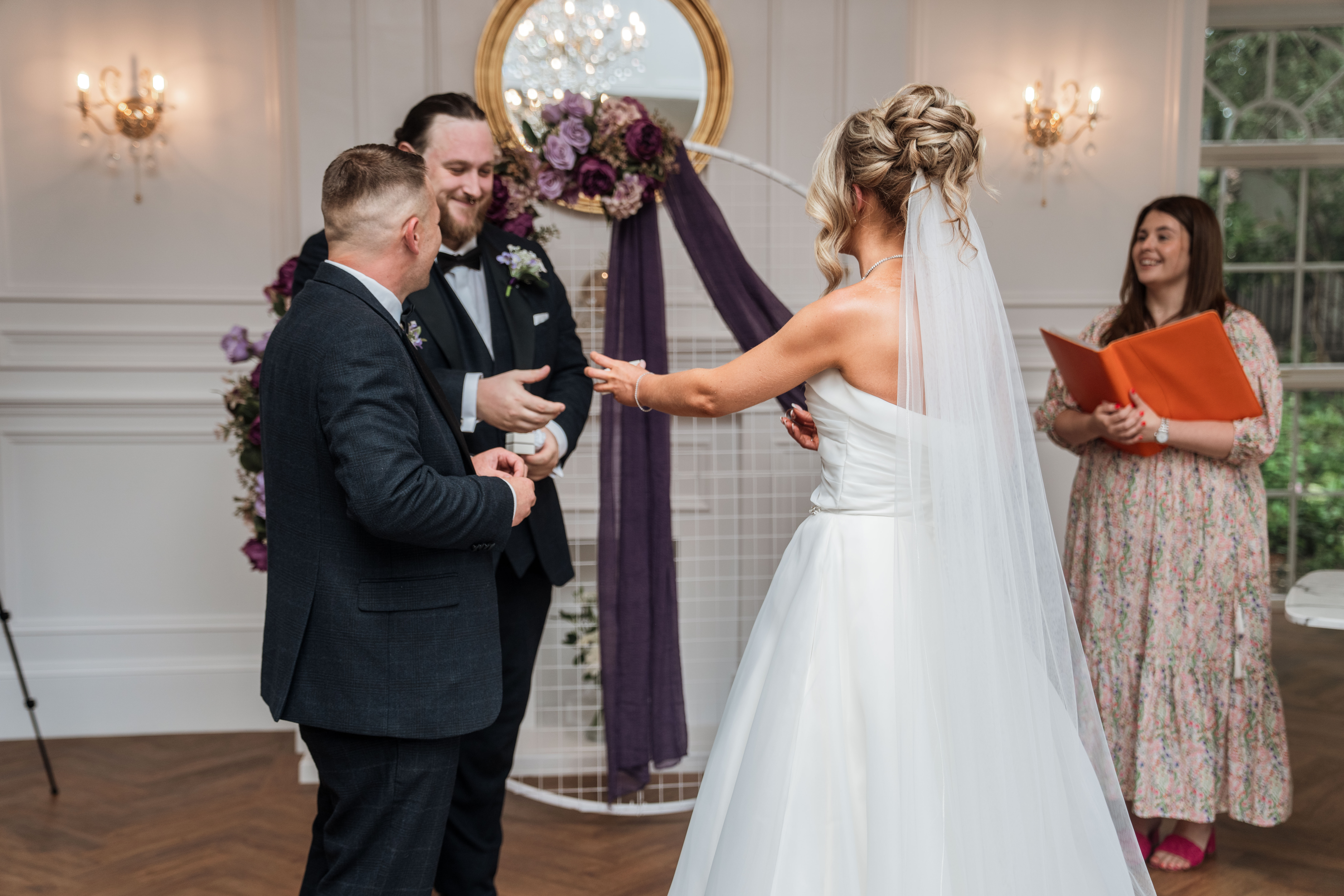 Bride and groom laughing during wedding ceremony with officiant holding book.