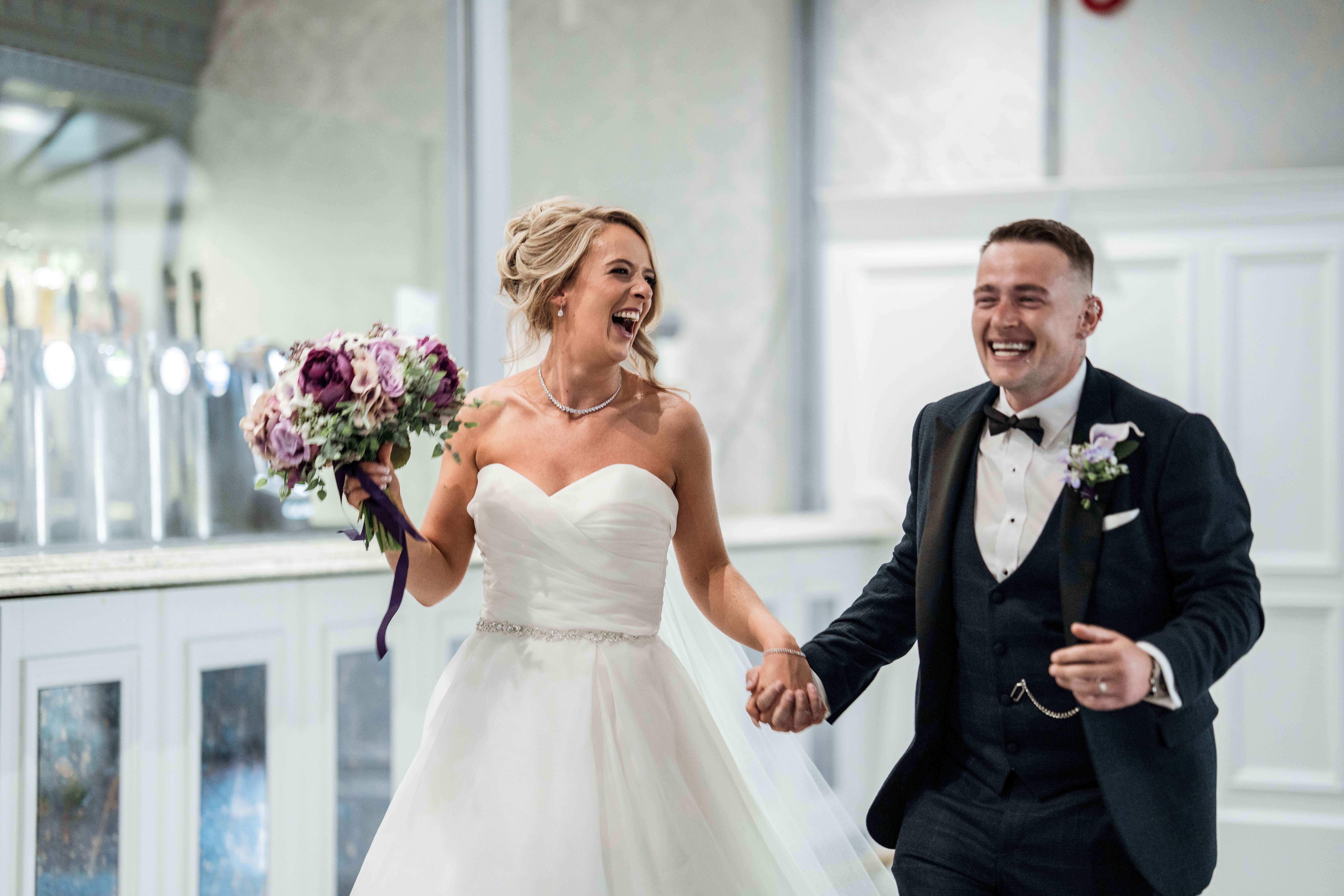 Bride and groom laughing joyfully, holding hands, with the bride holding a bouquet.