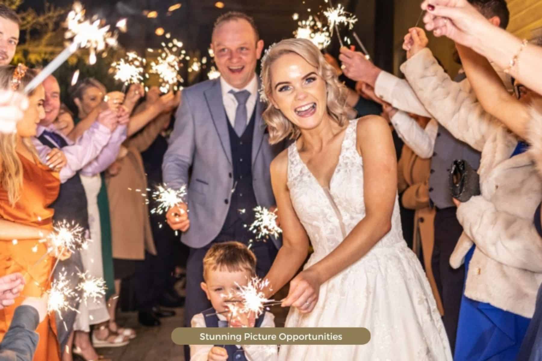 Bride and groom surrounded by wedding guests holding sparklers at a celebration.