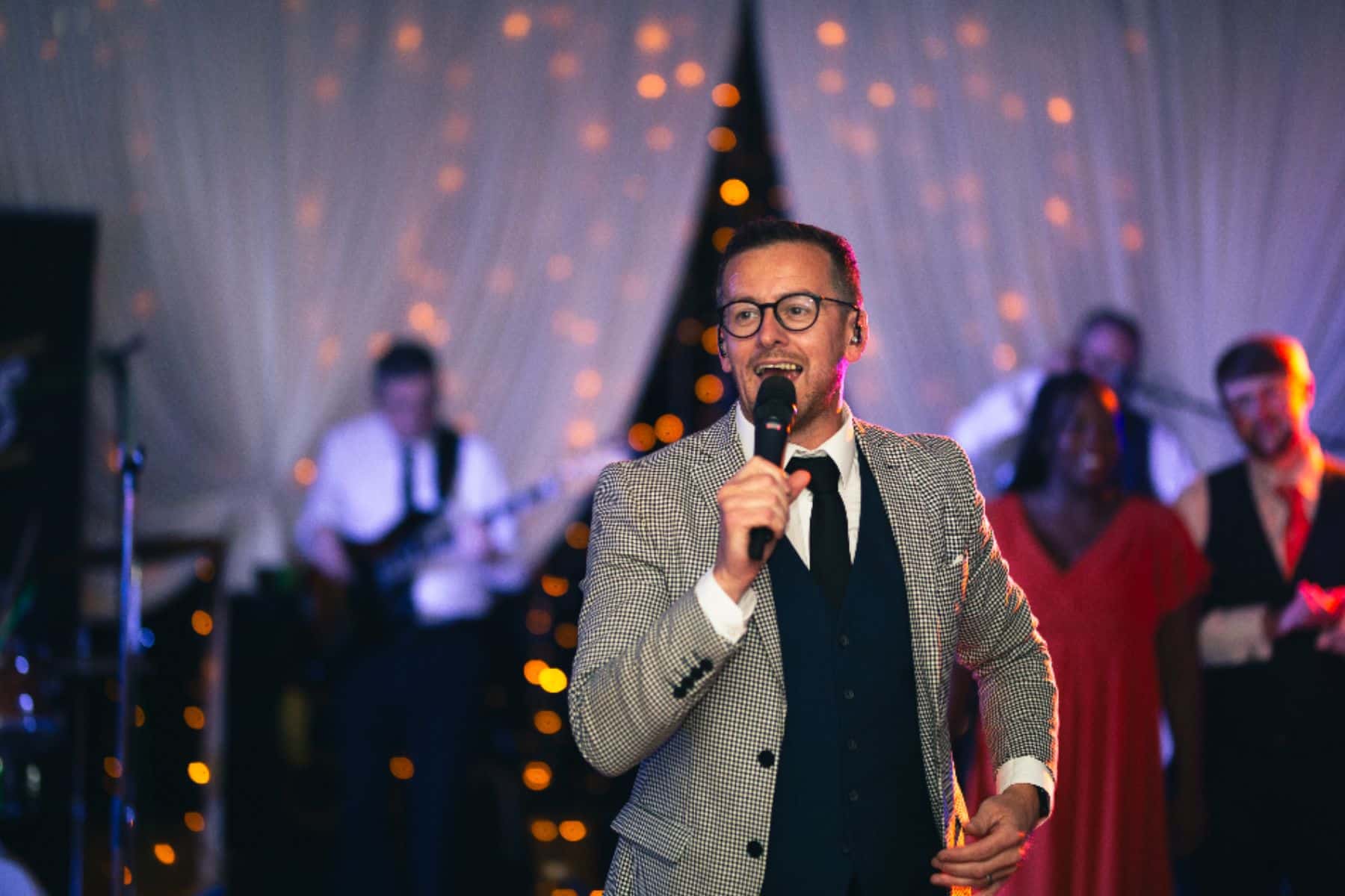 Man in a checkered suit singing into a microphone at a festive event.