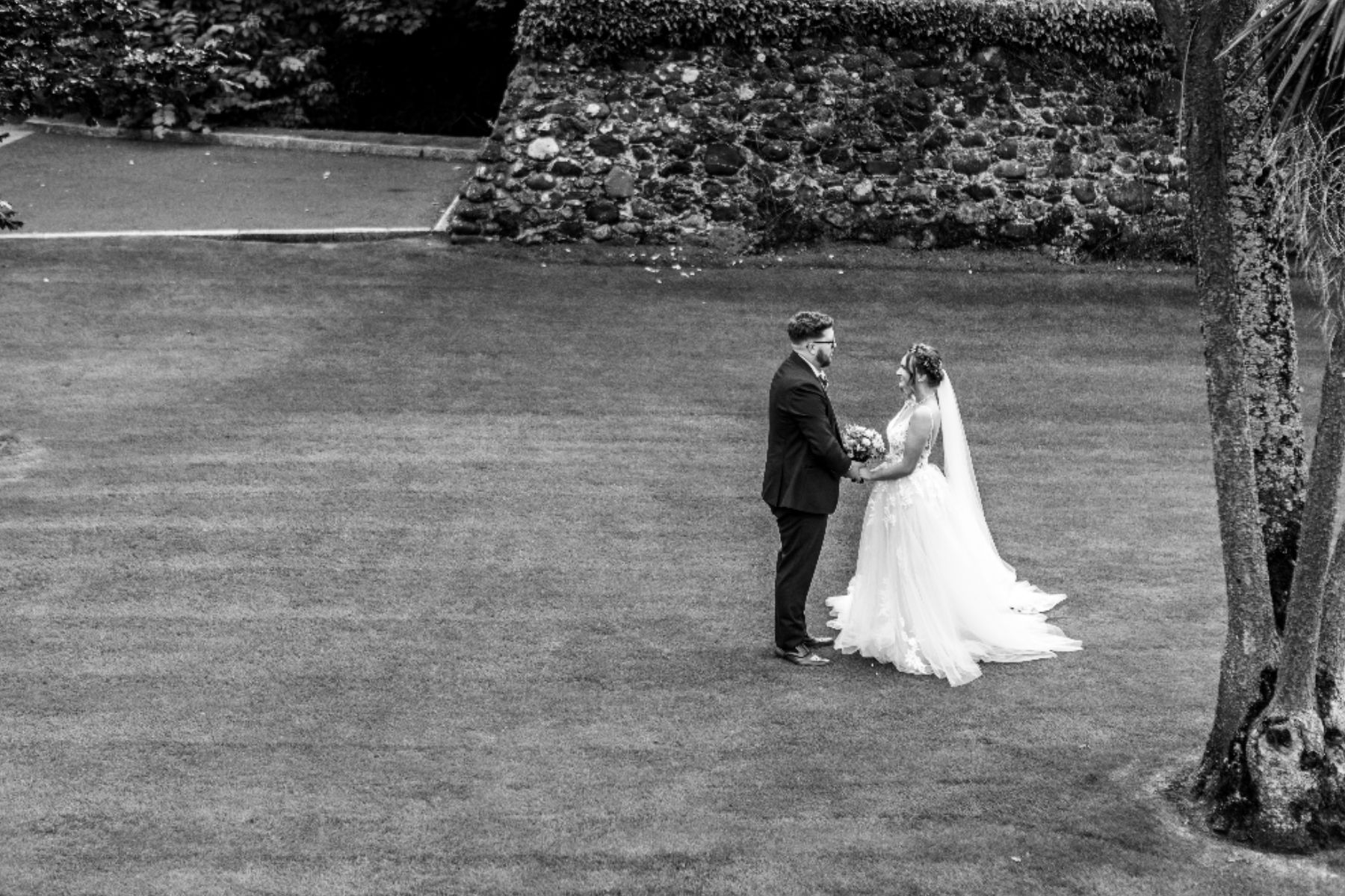 Bride and groom holding hands on grass in a black and white wedding photo.