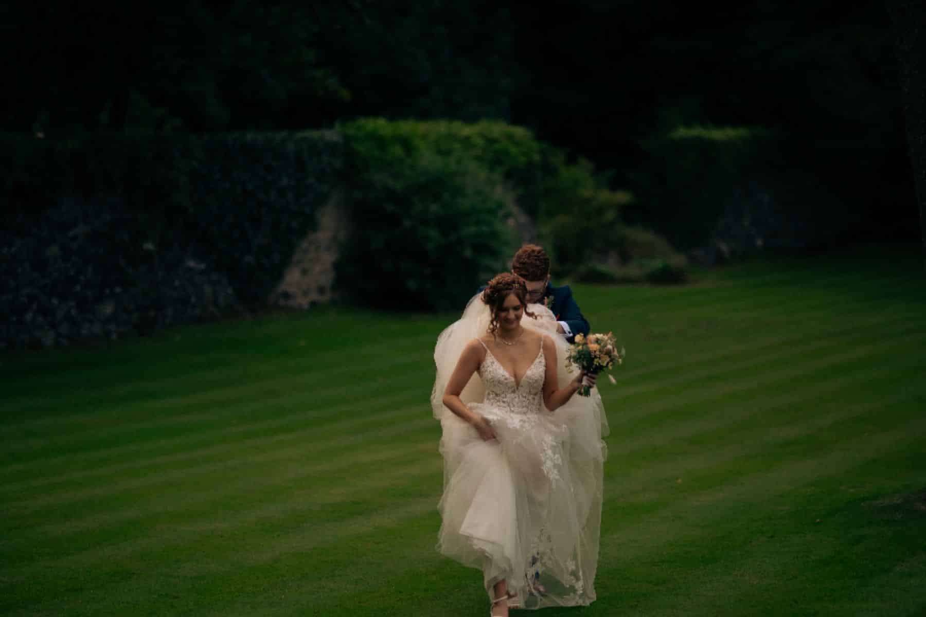 Bride and groom walking on a lush green lawn, the bride holding a bouquet.