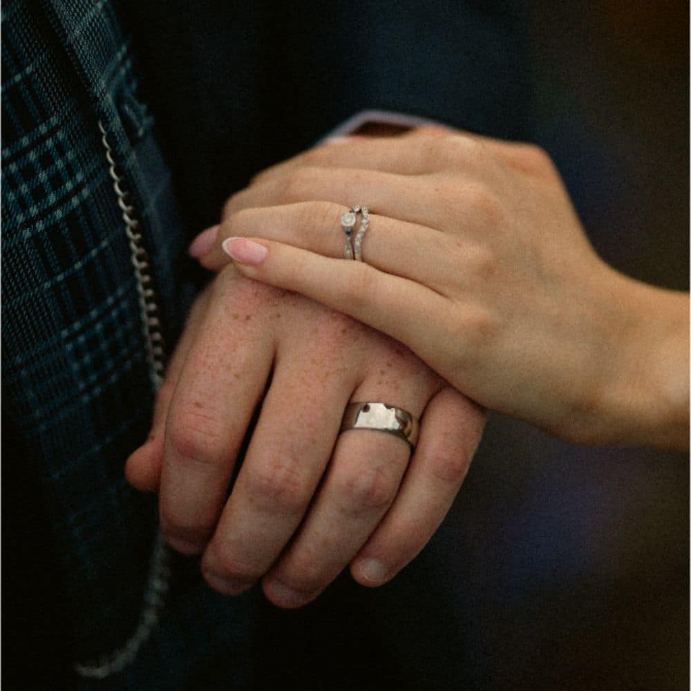 Hands with wedding rings, one with a diamond ring, the other with a silver band, symbolizing marriage or engagement.