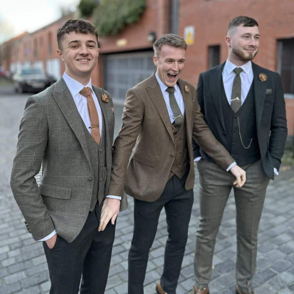 Three men in stylish suits laughing and standing on a cobblestone street.