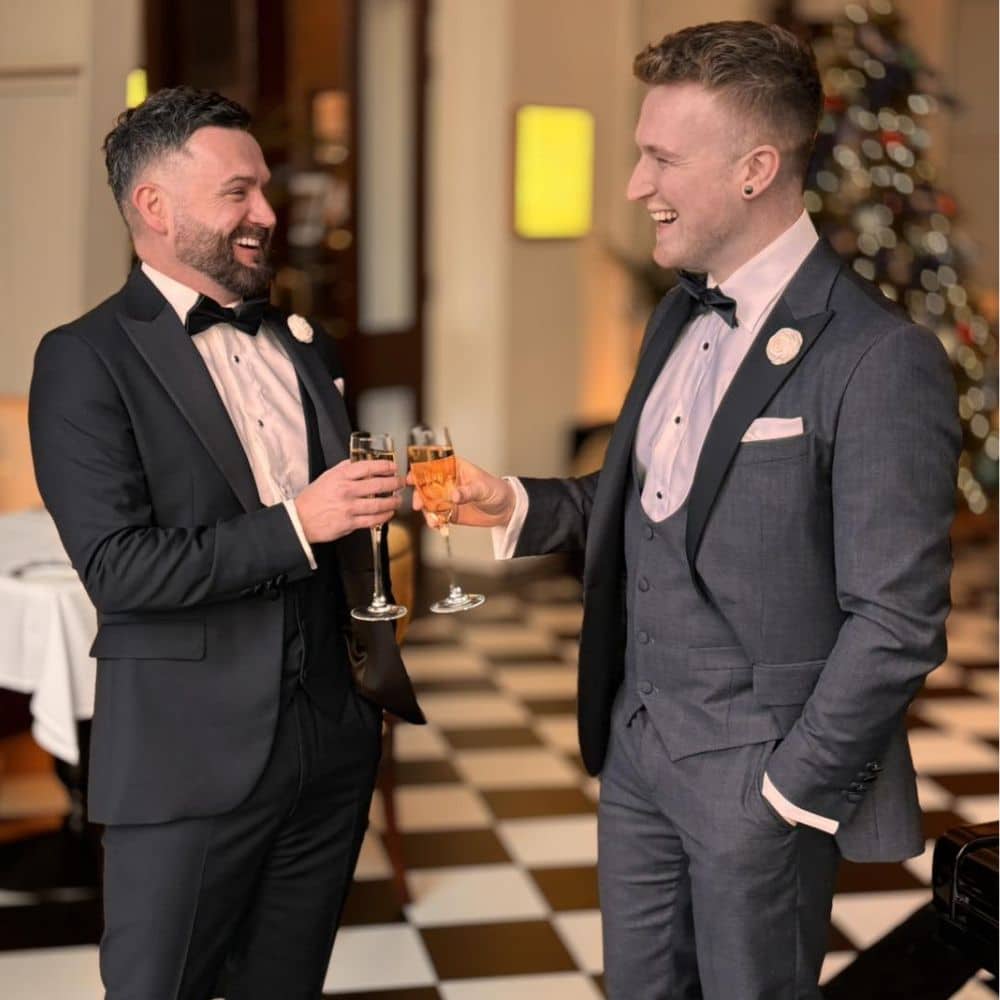 Two men in formal suits clinking glasses and smiling at each other in an elegant room.
