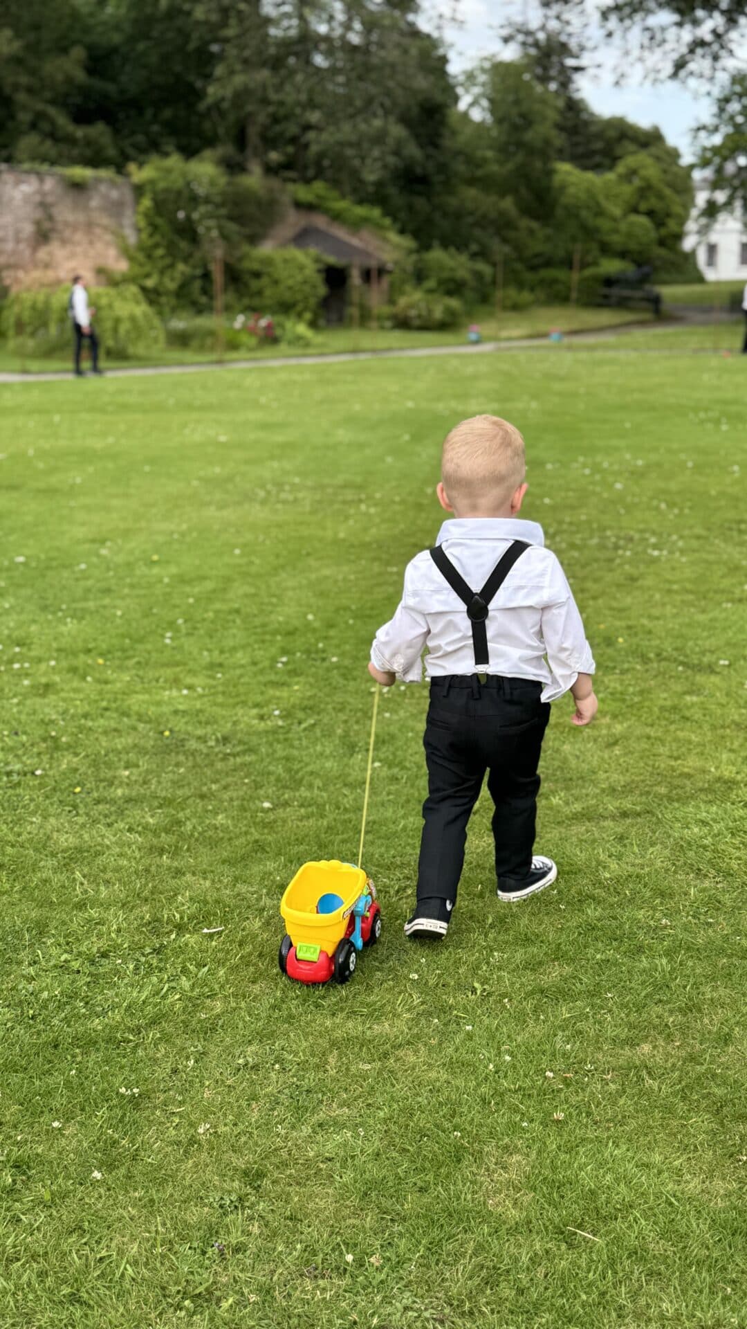 Toddler in formal wedding attire walking across the lawns at Ballyscullion Park in Northern Ireland, enjoying outdoor play during speeches at a child-friendly wedding.