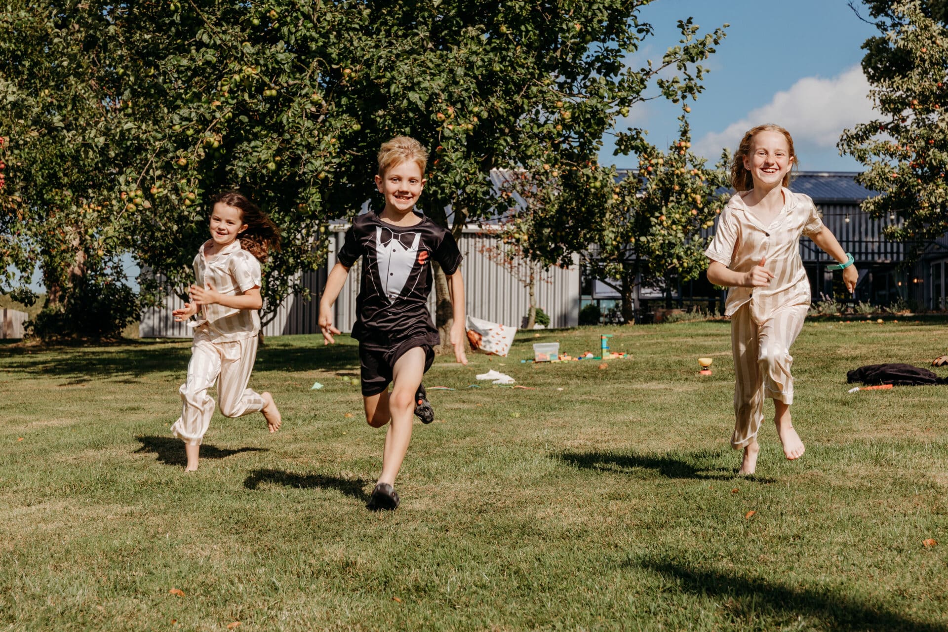 Children playing together outdoors during a wedding while parents enjoy the celebration.