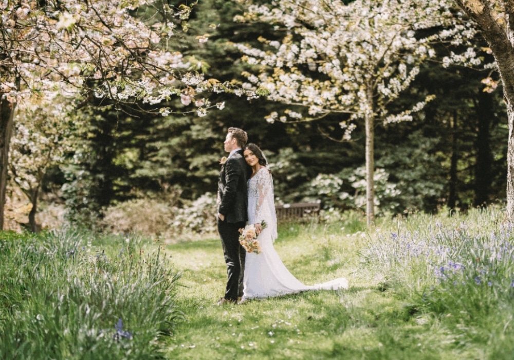 Bride and groom standing together in a lush garden with blooming trees.