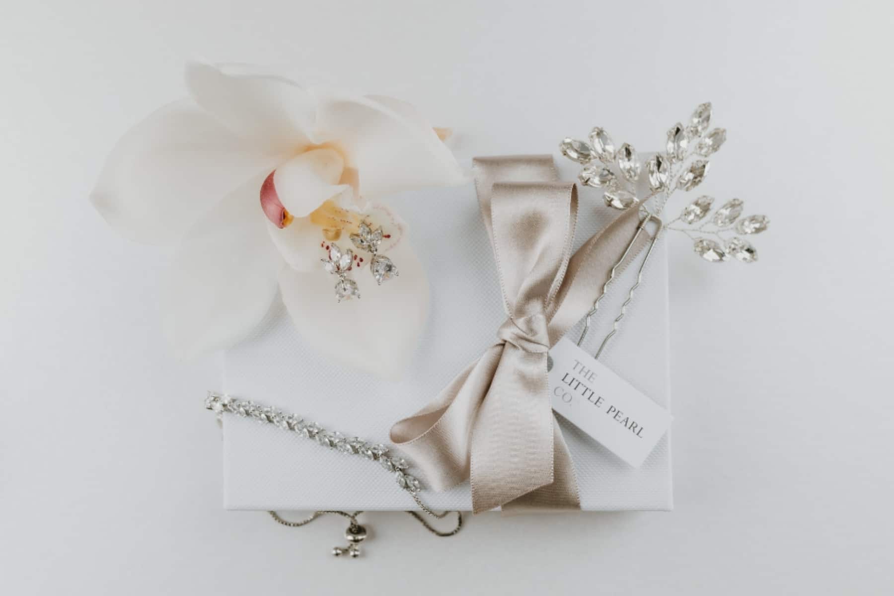 Elegant gift with satin bow, white orchid, and crystal hairpiece by The Little Pearl Company.