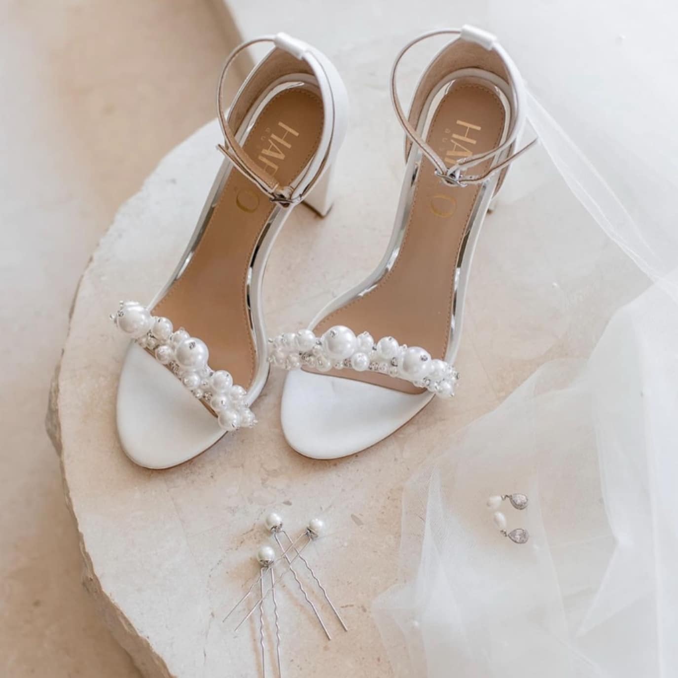 White bridal heels adorned with pearls, surrounded by pearl hairpins and earrings on a light surface.