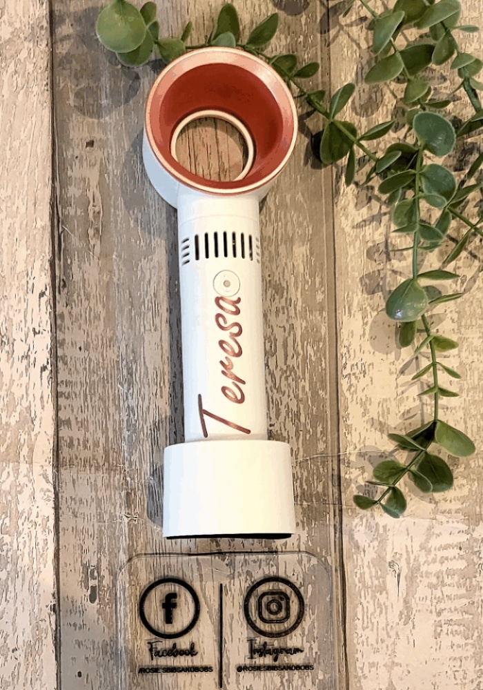 White hairdryer with "Teresa" label on a wooden surface with greenery; social media icons at the bottom.