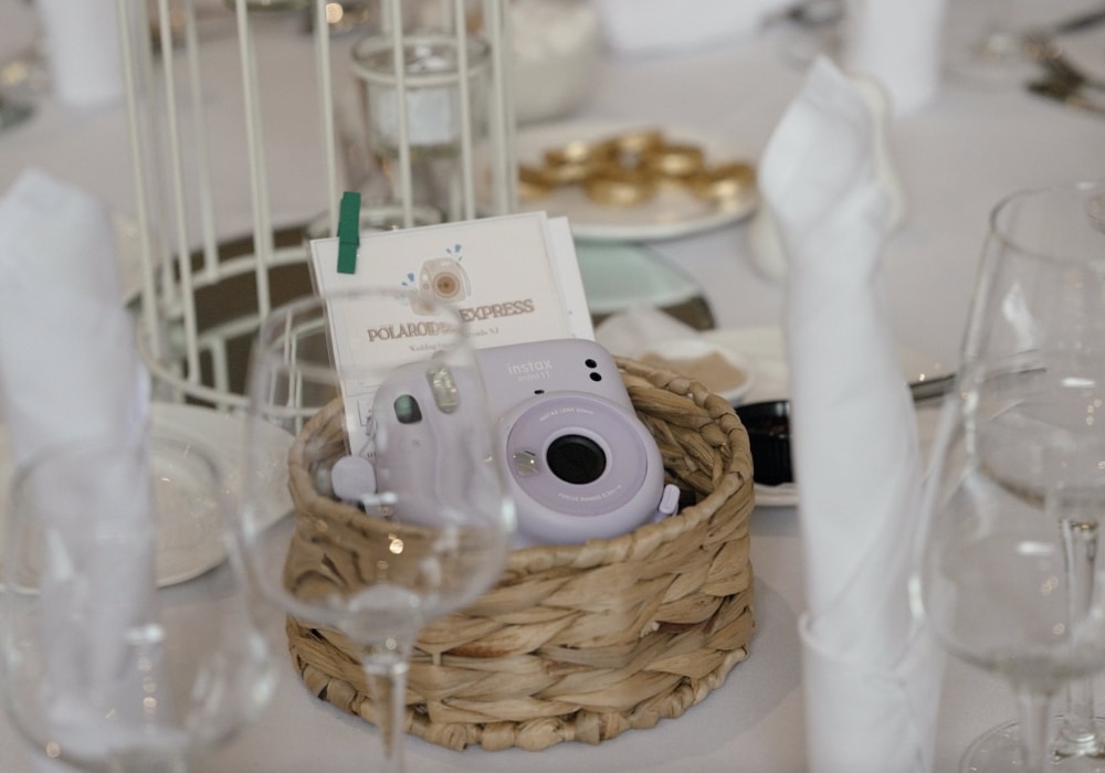 Purple Instax camera in a wicker basket on a decorated table with glasses and napkins.
