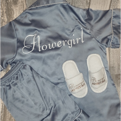 Blue silk pajama set embroidered with "Flowergirl" and matching slippers personalized with "Flowergirl Ahriyah" on wooden floor.