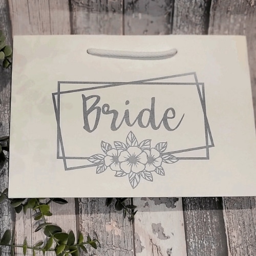 Cream bridal gift bag labeled "Bride" with floral design on rustic wooden background.